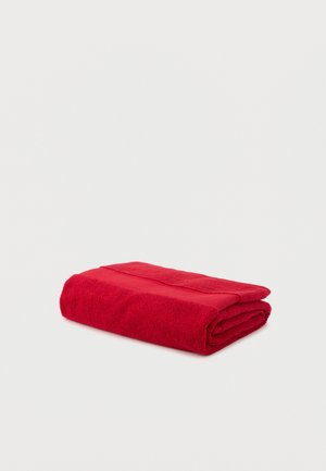 Serviette de bain rouge pliée en coton texturé sur fond blanc.
