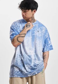 Blue gradient short-sleeve shirt with white floral patterns. Features a relaxed fit and a smooth, soft texture. Minor logo detail at the collar.