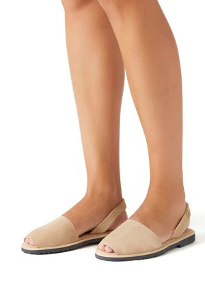 Zapatos de slingback de cuero beige con punta abierta, suela plana y un diseño simple. Presentan una textura suave y un detalle de costura minimalista.