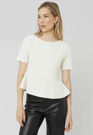 Haut peplum blanc en tissu texturé avec des manches courtes, un col rond et un bas évasé associé à un pantalon en cuir noir.