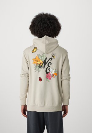 Haut à capuche beige avec des motifs floraux et d'insectes colorés dans le dos, avec un "NE" noir au centre. Poignets et ourlet côtelés.