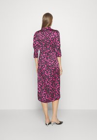 Zwarte jurk met een roze lipafdruk, met een getailleerde taille, driekwartmouwen en een middellange rok. Glad materiaal en een kraagdetail.