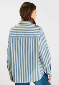Camicia a righe button-up in blu chiaro e crema. Presenta maniche lunghe, colletto e una vestibilità rilassata con un design a yoke sul retro.
