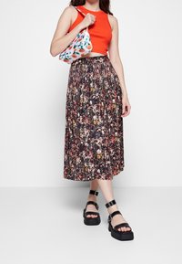 Rød cropped tank top, sort maxi nederdel med blomsterprint, sorte platform sandaler med remme og en multicolor håndtaske med frugtmønster.