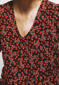 Vestito floreale con tessuto nero caratterizzato da motivi di fiori rossi e bianchi, scollatura a V e dettagli in superficie testurizzati.