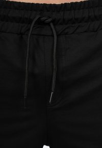 Shorts noirs à taille élastique avec cordon de serrage et embouts en plastique, texture de tissu lisse et détails de couture le long des côtés.