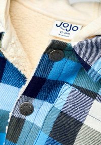 Camicia a scacchi in flanella blu, navy e verde con colletto foderato in sherpa crema. Presenta una chiusura a bottone e un'etichetta del marchio all'interno.