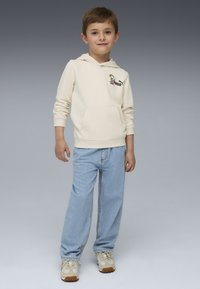 Felpa beige con tasca anteriore e logo stampato, abbinata a jeans a gamba dritta blu chiaro e sneakers beige e verdi.
