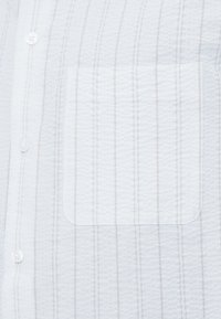 Λευκό πουκάμισο με υφή και κάθετες ανοιχτό γκρι ρίγες, με τσέπη στο στήθος και κουμπιά για κλείσιμο. Απαλό ύφασμα και χαλαρή σχεδίαση.