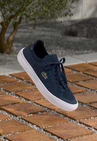 Tengerés kék sneaker, hálós felső résszel, kerek orral és gumitalppal. Az éltároló fűzőkkel és egy kis zöld logóval rendelkezik az oldalon.