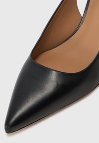 Černá kožená vysoká botka na podpatku s špičatou špičkou, hladkým povrchem a elegantním designem. Interiér má béžové kožené podšívku.