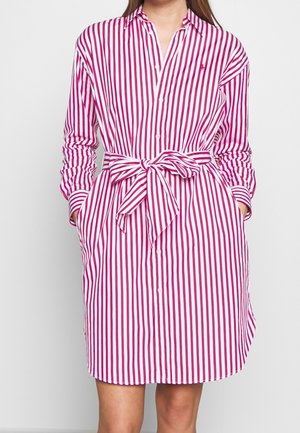 Robe chemise à rayures roses et blanches, avec des manches longues, une ceinture nouée à la taille et des poches latérales. Fabriquée en tissu léger.