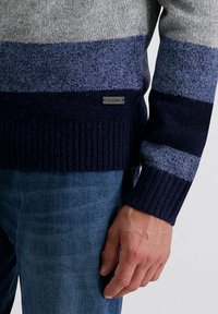 Heren gebreide trui met horizontale strepen in grijs, blauw en marineblauw, voorzien van een geribde zoom. Inclusief een klein logo-label aan de onderkant.