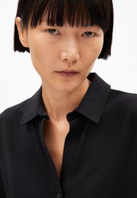 Black collared shirt with a smooth texture, featuring a button-up front and a structured collar design. Close-up view of the shirt.