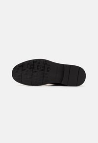 Semelle de chaussure en caoutchouc noir avec un motif texturé, comprenant des rainures horizontales et un design en blocs stylisé. Surface lisse avec un léger brillant.