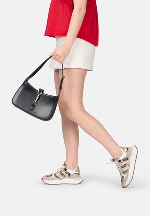 Borsa a tracolla nera in pelle con hardware dorato, tenuta con una mano. Il modello indossa un top rosso, una gonna bianca e sneakers con stampa leopardata.