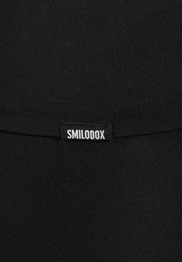 Schwarzer Stretchstoff mit einer glatten Textur, ausgestattet mit einem kleinen weißen Etikett, auf dem "SMILODOX" steht, in der Nähe der oberen Kante. Einfaches und einheitliches Design.