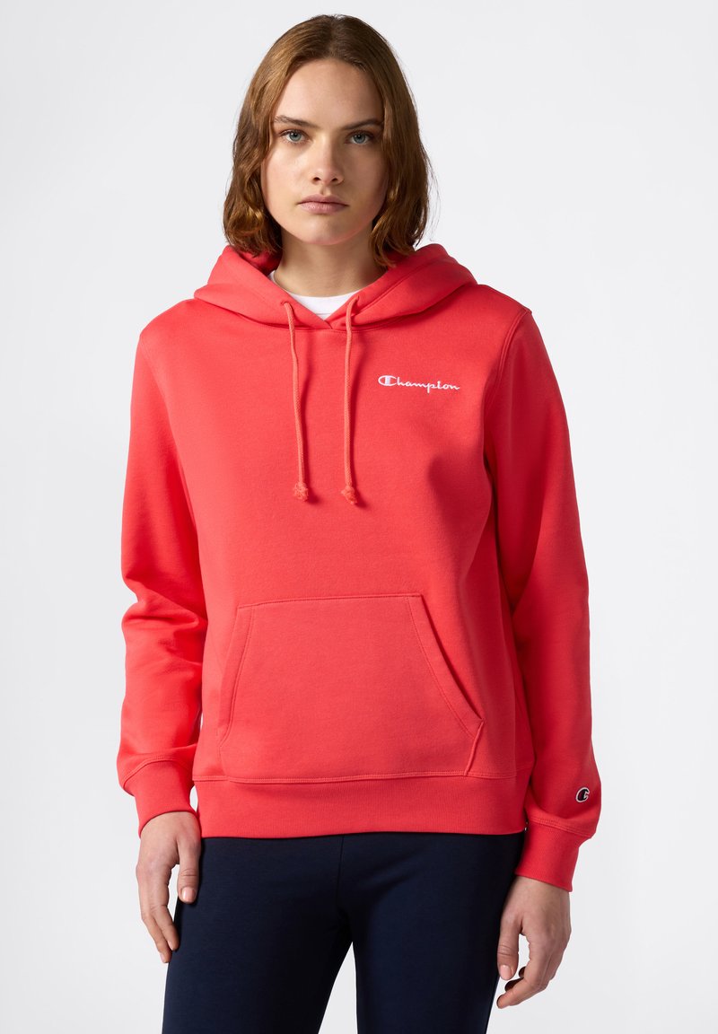 Sudadera con capucha roja hecha de una tela suave y texturizada, con un bolsillo frontal y cordones. Presenta un logo de Champion en blanco en el pecho.
