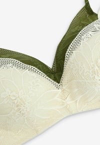 Verkkopitsinen bralette, jossa on oliivinvihreä yläosa ja kermaisenvalkoinen alaosa, kukkakuviot ja teksturoidut reunat. Mukana säädettävät olkaimet.
