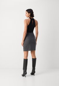 Zwarte mouwloze bodysuit met een keyhole rug, gecombineerd met een aansluitende grijze rok en kniehoge zwarte laarzen van soepel leer.