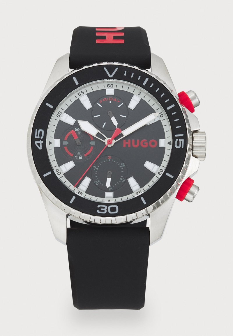 Black rubber strap watch with silver stainless steel case. Round black dial features red accents, chronograph subdials, and date display.