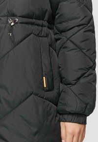 Zwarte pufferjack met een ruitpatroon. Voorzien van een verstelbare trekkoord in de taille, elastische manchetten en een zijzak met een merketiket.