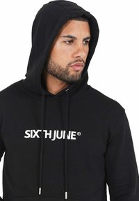 Sudadera de algodón negra con bolsillo canguro delantero, cordones y un logo bordado en blanco "SIXTHJUNE" en el pecho.
