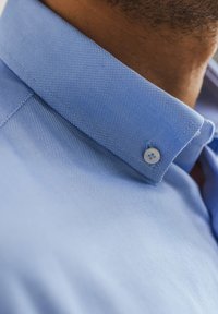 Lichtblauw shirt met een gestructureerde kraag, textuurstof met een subtiel patroon en een knoopdetail op de kraag.