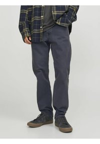 Camisa de franela de cuadros en tonos marinos sobre una camiseta gris, combinada con jeans rectos de color gris oscuro y zapatillas negras. Conjunto casual con detalles de tela texturizada.