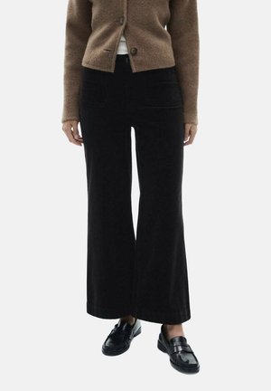 Pantalons en velours côtelé noir à jambes larges avec une texture douce, dotés de poches avant et d'une taille ajustée, associés à un cardigan marron.