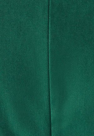 Tessuto verde con una superficie testurizzata e una finitura liscia. La superficie appare leggermente lucida, con una cucitura visibile che corre verticalmente lungo il centro.