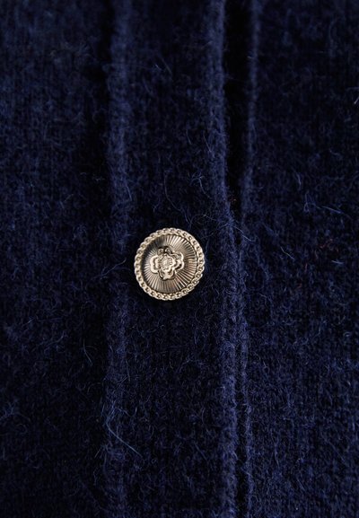 Navy textured fabric with a gold decorative button featuring floral design and ribbed border, positioned on a vertical seam.