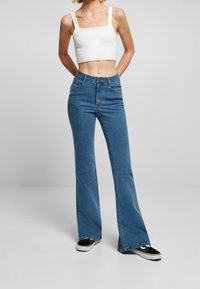 Jeans de mezclilla de tiro alto en un tono azul claro y de corte acampanado, combinados con una camiseta blanca corta y zapatillas negras. Presenta detalles de costura.
