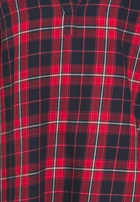 Chemise à carreaux rouges et bleu marine avec un tissu doux, un petit plastron, et des lignes horizontales et verticales blanches et grises dans le motif.