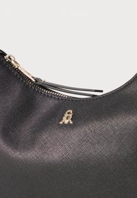 Borsa in tessuto nero con texture liscia, caratterizzata da un accento logo dorato, chiusura a zip e sottili cinturini decorativi.