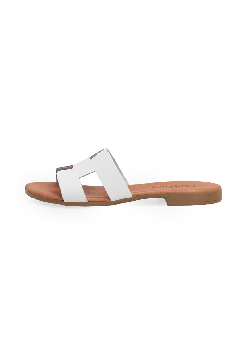 Hvide flade sandaler med to brede stropper, der har et geometrisk udsnitdesign, læderoverdel og en brun sål. Minimalistisk stil og glat tekstur.