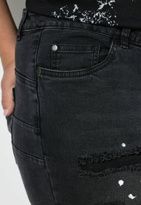 Zwarte denim jeans met een slim fit, vijf-pocket ontwerp en gescheurde details met rafelige randen en witte verfspetters.