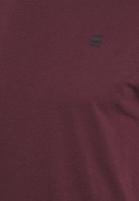 Bordowa koszulka z krótkim rękawem, wykonana z miękkiej bawełny, z okrągłym dekoltem i czarnym logo nadrukowanym na piersi.