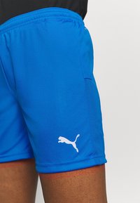 Blå sportshorts gjorda av lättviktsmaterial med en slät textur, med mesh-detaljer och en vit logotyp på vänster sida.