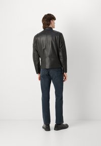 Black leather jacket with angled shoulders, quilted accents on sleeves, and a high collar. Worn with dark jeans and black shoes.