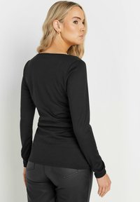 Czarna koszula z długim rękawem, dopasowana z okrągłym dekoltem, wykonana z miękkiego materiału. Stylizowana z eleganckimi spodniami, z minimalnymi detalami z tyłu.