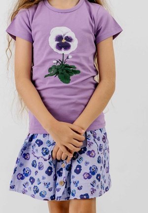 Child wearing a purple t-shirt with a large white and purple flower print and a matching skirt with a small floral pattern and buttons.