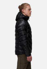 Svart puffjacka med huva, med kviltat mönster och en slät, glänsande yta. Sidofickor med dragkedja synliga. Slim fit-stil.