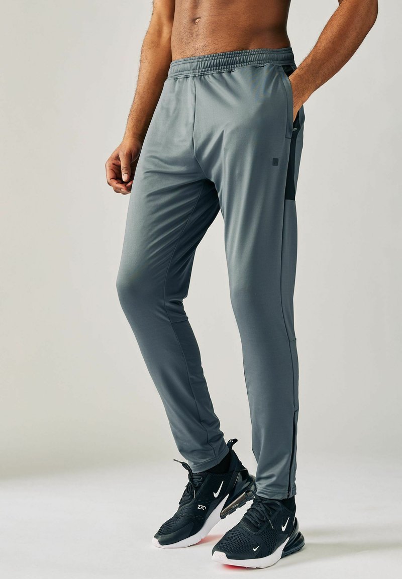 Šedé sportovní kalhoty slim fit s elastickým pasem a bočními kapsami. K tomu černé tenisky s bílými detaily.