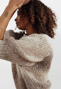 Lekki sweter dziany w beżowych i brązowych odcieniach. Cechuje się luźnym, teksturowanym materiałem o przytulnym, oversize'owym kroju i ściągaczami przy mankietach.