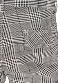 Schwarz-weiße Karomuster-Latzhose aus strukturiertem Stoff, mit einer Tasche mit diagonalen Streifen und kontrastierenden Nähten.