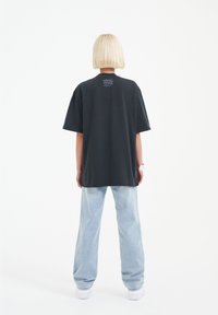 Black oversized t-shirt featuring short sleeves, a rounded neckline, and a small graphic print on the upper back. Paired with light blue jeans.