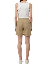 Beige shorts met een elastische tailleband, omgeslagen mouwen en twee achterzakken, gecombineerd met een witte tanktop die een minimalistisch design toont.