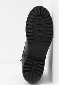 Semelle de botte noire avec une bande de roulement texturée pour l'adhérence, présentant des rainures prononcées et un marquage de taille "37" embossé sur le côté.