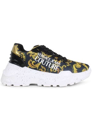 Sneaker Versace Jeans Couture avec un dessus noir orné d'un motif baroque doré, une semelle blanche tachetée et un logo prononcé sur le côté.